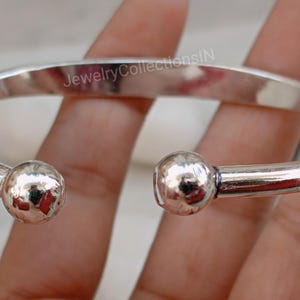 May include: Silver bangle bracelet with two round, textured ends. The bracelet is open and has a simple, minimalist design.