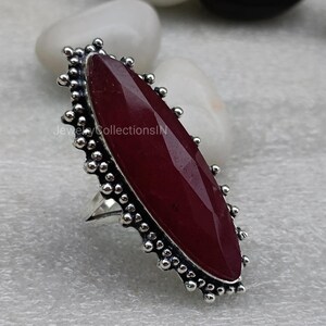 May include: A silver ring featuring a large, oval-shaped, dark red gemstone set in a beaded bezel. The ring has a simple band.