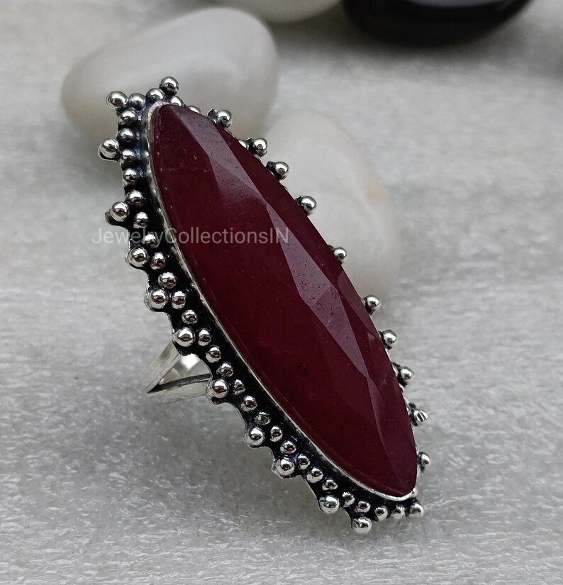 May include: A silver ring featuring a large, oval-shaped, dark red gemstone set in a beaded bezel. The ring has a simple band.