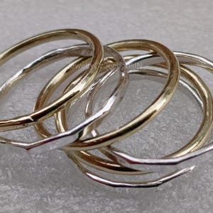May include: Five simple stacking rings, two gold and three silver, with a hammered texture. The rings are stacked on top of each other.