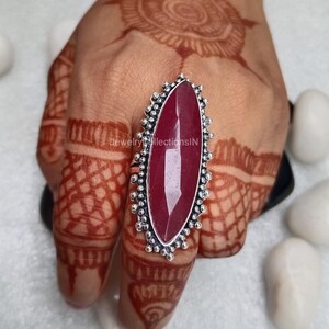 May include: A silver ring featuring a large, oval-shaped, red gemstone. The ring has a decorative, beaded design around the stone.