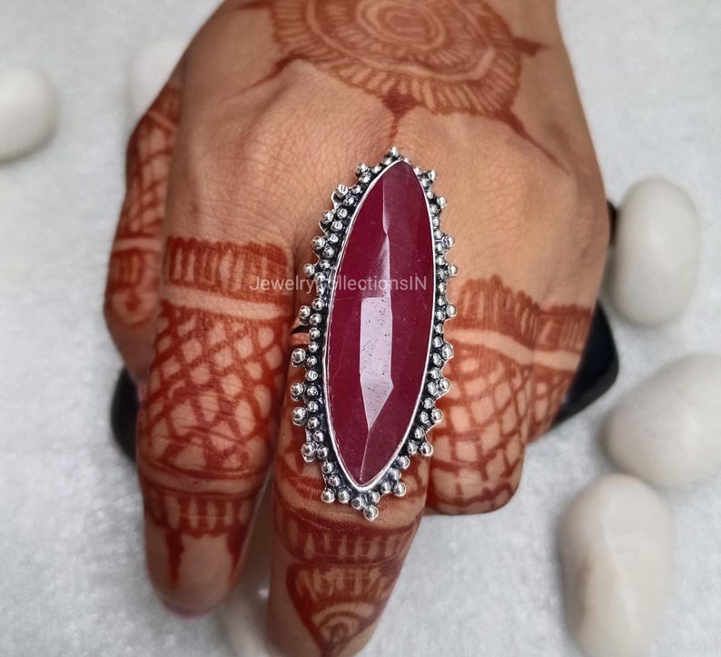 May include: A silver ring featuring a large, oval-shaped, red gemstone. The ring has a decorative, beaded design around the stone.