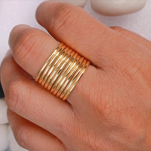 May include: A stackable gold ring set. The rings are smooth, shiny, and round, creating a bold statement. The rings are worn on a finger, showcasing their simple yet elegant design. The gold color adds a touch of luxury.