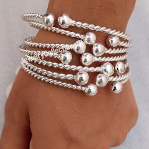 May include: A set of five silver bangle bracelets with a twisted rope design and small round beads. The bracelets are stacked on top of each other on a person's wrist.