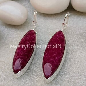 May include: A pair of silver dangle earrings with a deep red oval-shaped gemstone. The earrings have a simple design and are perfect for everyday wear.
