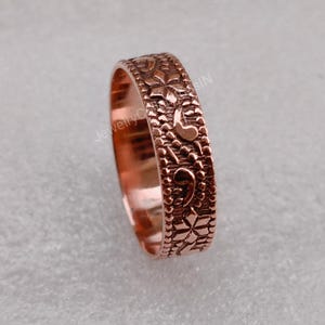 May include: A copper band ring with an intricate floral design. The ring is polished and has a smooth finish.