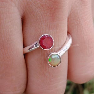 Peut inclure: Une bague en argent avec une pierre précieuse rouge et une opale blanche. La bague est conçue pour s'enrouler autour du doigt.