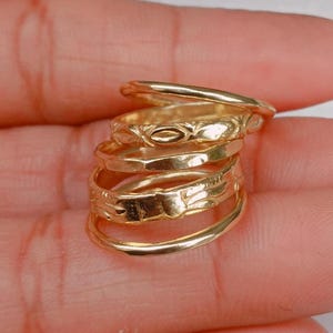 May include: A collection of gold rings, each with a distinct design. The rings have varying widths and feature embossed patterns, including floral and geometric shapes. The rings are stacked, highlighting their intricate details and golden shine.