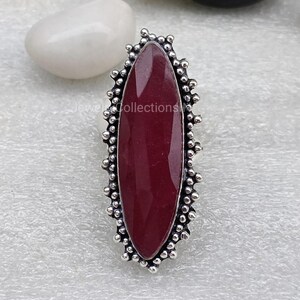 May include: A silver ring featuring a dark red oval gemstone set within a decorative border of small silver beads.