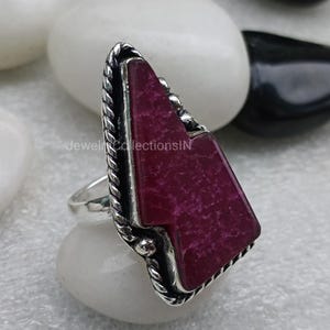 Könnte beinhalten: Ein silberner Ring mit einem großen, unregelmäßig geformten Edelstein in dunkelvioletter Farbe, der in einer silbernen Fassung sitzt. Der Ring hat ein dekoratives, gedrehtes Silberband.