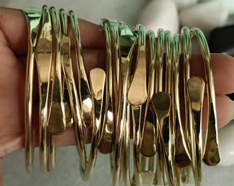 Peut inclure: Un ensemble de 12 bracelets en métal doré avec un design unique en forme de larme. Les bracelets sont empilés et disposés dans une main, mettant en valeur leurs détails complexes.