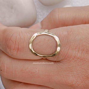 Peut inclure: Une bague dorée avec un design ovale. La bague a une texture martelée et est portée au doigt. La bague est un bijou.