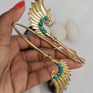May include: A gold bangle bracelet with two wing-shaped ends. Each wing is decorated with turquoise gemstones.
