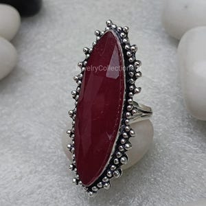 May include: A silver ring featuring a large, oval-shaped, dark red gemstone set within a decorative, beaded border.