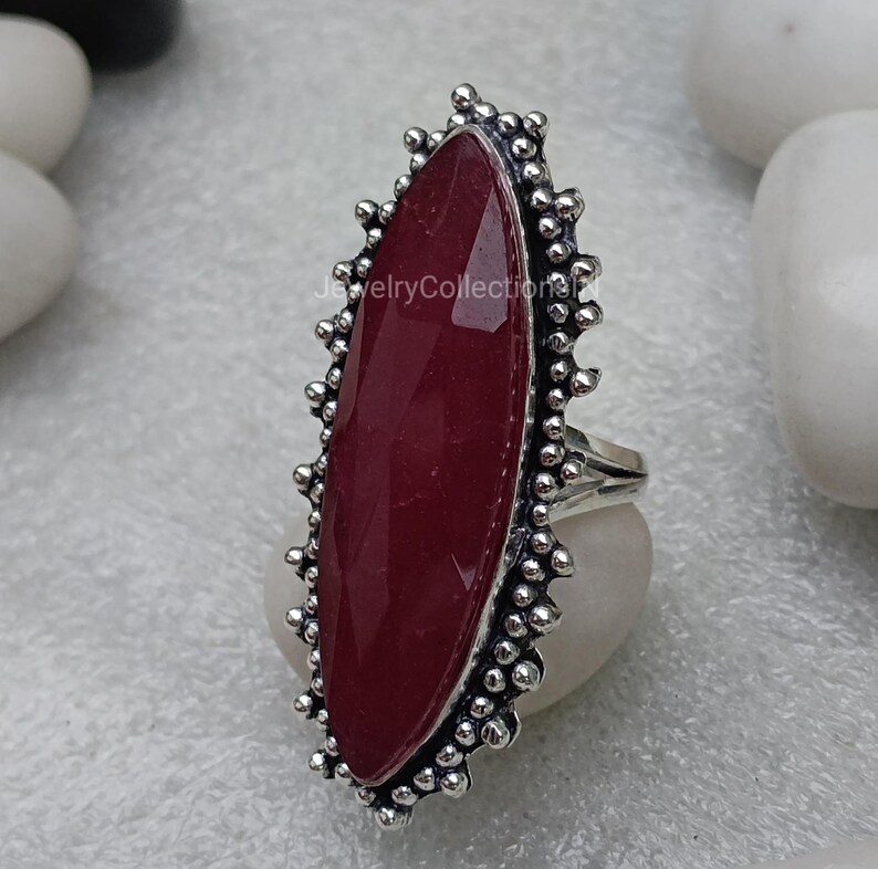 May include: A silver ring featuring a large, oval-shaped, dark red gemstone set within a decorative, beaded border.