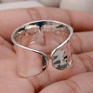 Könnte beinhalten: Ein offener Silberring mit gehämmerter Textur. Der Ring ist breit und hat eine leicht gebogene Form.