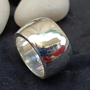 May include: A wide silver band ring with a smooth, polished finish. The ring is thick and has a rounded shape.