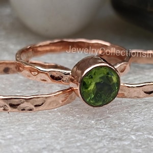 May include: Two hammered rose gold rings with a green peridot gemstone. The rings are stacked on top of each other.