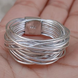 Può includere: Un anello d'argento con un design intrecciato. L'anello è realizzato con più fili di filo d'argento intrecciati per creare un motivo unico e intricato.