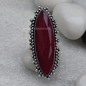 May include: A silver ring featuring a large, oval-shaped, dark red gemstone set within a decorative, beaded border.