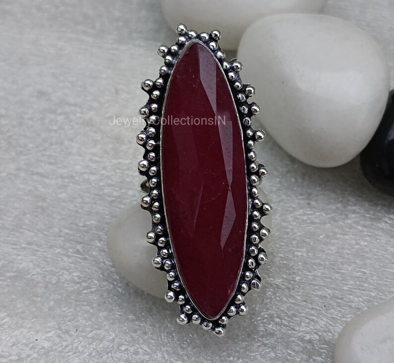 May include: A silver ring featuring a large, oval-shaped, dark red gemstone set within a decorative, beaded border.