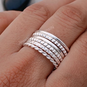 May include: A set of seven silver stacking rings with different textures, including a twisted band, a hammered band, and a beaded band.