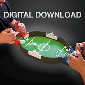 May include: A tabletop soccer game with a green playing field, white markings, and small white soccer balls. The game has red and blue handles with white control knobs. The text "DIGITAL DOWNLOAD" is displayed in white.