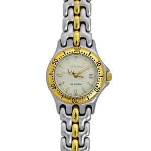 May include: A two-tone gold and silver wristwatch with a white face and black markings. The watch has a gold bezel with black markings and the words "100 METERS" printed on the face. The watch has a two-tone gold and silver band.