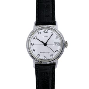 Könnte beinhalten: Eine silberne Timex-Uhr mit weißem Zifferblatt und schwarzem Lederarmband. Die Uhr hat schwarze arabische Ziffern und ein Datumsfenster bei 3 Uhr. Das Zifferblatt der Uhr trägt außerdem die Aufschrift "Water Resistant".