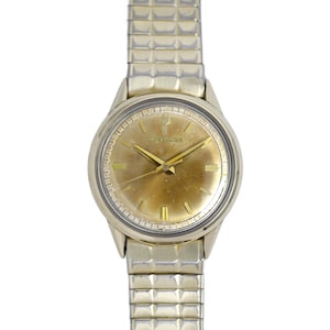 May include: A gold-toned wristwatch with a round face and a gold-toned metal band. The watch face has a gold-toned dial with black hour and minute hands and a black second hand. The watch face also has black Roman numeral hour markers and a small black second hand dial at the 6 o'clock position. The watch face has the word "Bulova" printed in black at the 12 o'clock position.