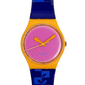Puede incluir: Un reloj Swatch amarillo y azul con una esfera rosa y agujas naranjas. El reloj tiene el logotipo de Swatch en la esfera.