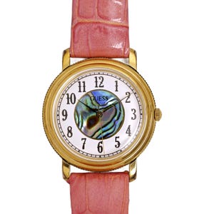 May include: A gold-tone wristwatch with a white face and black hands. The watch has a mother-of-pearl dial with a blue and green iridescent pattern. The watch has a pink leather strap with a crocodile pattern. The watch face says "GUESS" in black lettering.