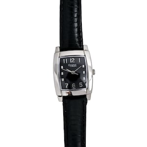 Puede incluir: Un reloj Caravelle by Bulova plateado con una correa de cuero negro y una esfera negra. El reloj tiene una forma rectangular y un bisel plateado.