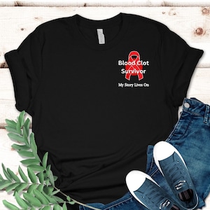 Op de afbeelding: Zwart T-shirt met een rood lint en de tekst "Blood Clot Survivor" en "My Story Lives On".