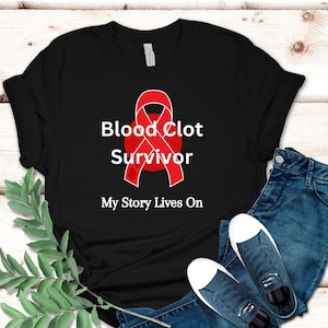 Op de afbeelding: Zwart T-shirt met een rood lint en de tekst "Blood Clot Survivor My Story Lives On".