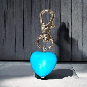 Könnte beinhalten: Ein türkisfarbener herzförmiger Anhänger, der an einem silbernen Schlüsselanhänger mit einem Karabinerhaken befestigt ist.