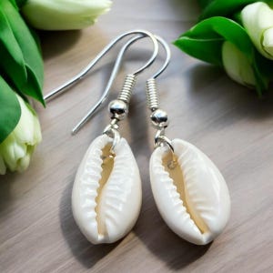 May include: A pair of white shell earrings with silver hooks. The shells are oval shaped and have a textured surface.