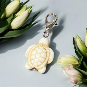 May include: White ceramic turtle charm with a silver lobster clasp. The turtle has a detailed shell with a textured surface.