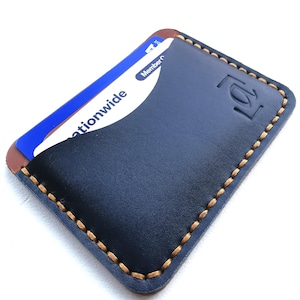 May include: A navy blue leather card holder with a brown interior and tan stitching around the edges. A credit card is partially visible, with the word "nationwide" printed on it. The card holder has a debossed logo.