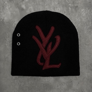 May include: A black knit beanie featuring a large, dark red embroidered monogram logo of the letters YL centered on the front. The beanie includes two small, circular silver-toned metal eyelets positioned vertically on the left side panel.