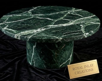 Puede incluir: Una mesa redonda de mármol verde con vetas blancas. La mesa tiene una base cilíndrica y una tapa circular. La mesa está hecha de mármol pulido y está colocada sobre un fondo negro. La mesa es una pieza decorativa. El letrero dice "ROYAL INLAY CREATIONS".