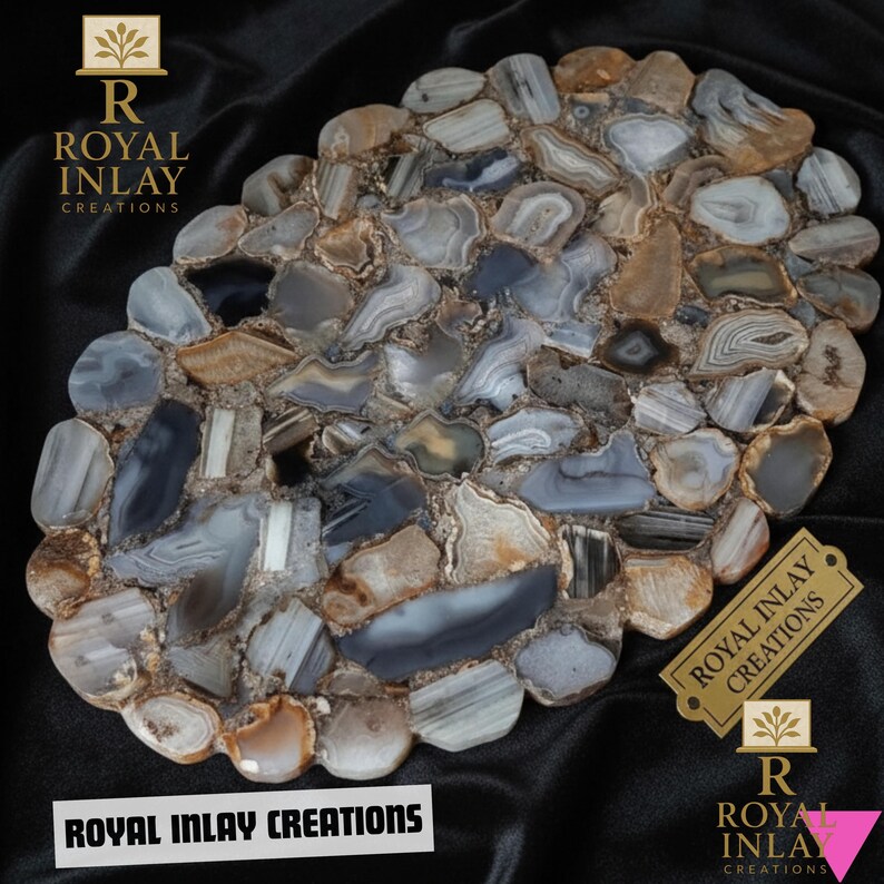 Puede incluir: Pieza decorativa ovalada de piedra compuesta por piedras de &aacute;gata grises, marrones y blancas. La superficie es un mosaico de formas irregulares. El texto "ROYAL INLAY CREATIONS" se muestra en la parte inferior y en una etiqueta dorada.