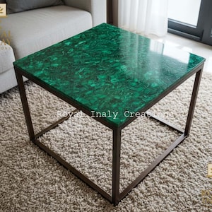 Può includere: Tavolino quadrato con un piano in malachite verde vibrante e una struttura in metallo scuro. Il tavolo ha un design moderno ed è adatto per un soggiorno o un'area lounge. Il tavolo è un elemento decorativo.