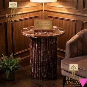 Puede incluir: Una mesa auxiliar redonda con tapa de mármol rojo y base cilíndrica estriada. La mesa tiene un letrero que dice "Royal Inlay Creations". La mesa está en una habitación con paneles de madera y una silla de terciopelo.