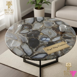 May include: Circular coffee table featuring a striking agate stone surface in grey, white, and black hues. It has a black metal base and a small white cup. The table is from Royal Inlay Creations.