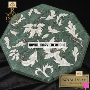 May include: Green marble tabletop with inlaid floral design. The octagonal table features white and brown accents in a symmetrical pattern. The text "ROYAL INLAY CREATIONS" is displayed on the table and a gold plaque.