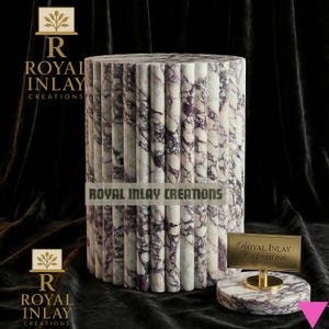 Può includere: Un tavolino cilindrico in marmo con un design scanalato, con venature bianche e viola. Il tavolo è accompagnato da un pezzo di marmo più piccolo e abbinato con un cartello dorato che recita "Royal Inlay Creations".