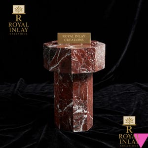 Può includere: Un tavolino esagonale realizzato in marmo rosso intenso con venature bianche prominenti. Il tavolo presenta un piano spesso e piatto e una robusta base esagonale abbinata. Una piccola targa dorata riporta ROYAL INLAY CREATIONS.