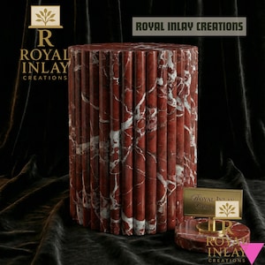Può includere: Un tavolino cilindrico in marmo rosso con venature bianche. Il tavolo ha un design scanalato ed è accompagnato da un espositore più piccolo abbinato. Il testo "ROYAL INLAY CREATIONS" è visibile.