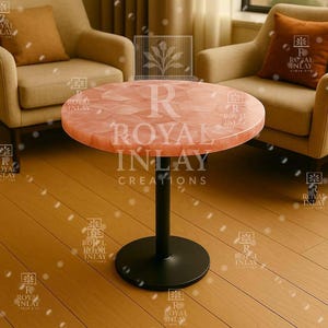 May include: A round, pink, table with a black metal base. The table top is made of natural stone with a unique, textured surface. The table is labeled "R Royal Inlay Creations".